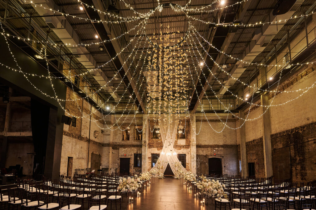 thousands of paper cranes hang from the ceiling with strands of lights over a wedding ceremony space in Aria