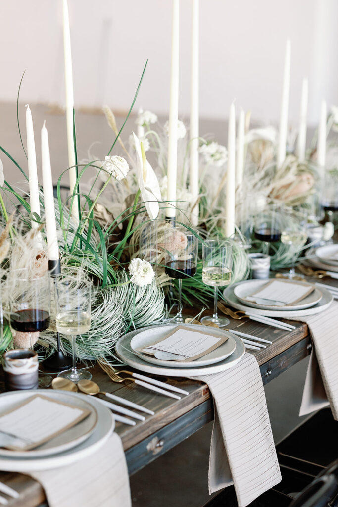 organic tablescape design with wild grasses and large candlesin the center with wine glasses and natural wood tabletop