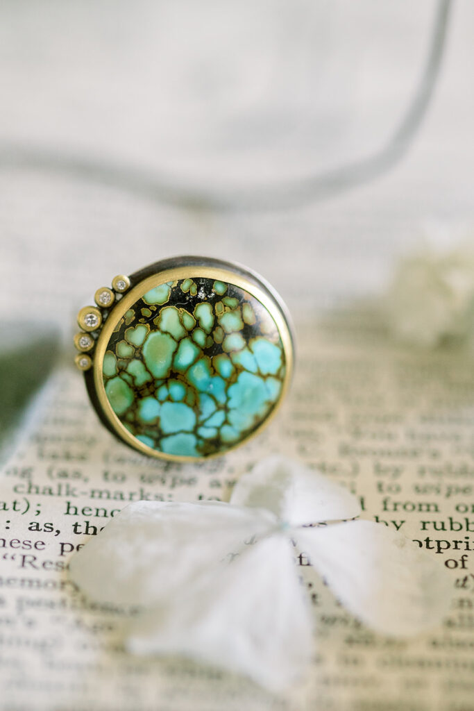 diamond-accented turquoise wedding ring sitting atop a book with flower petals