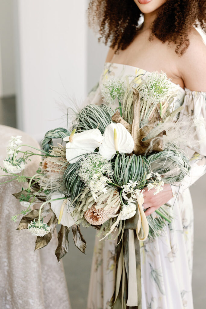 bride holding delicate bridal floral arrangement with braided grasses and white and blush flowers